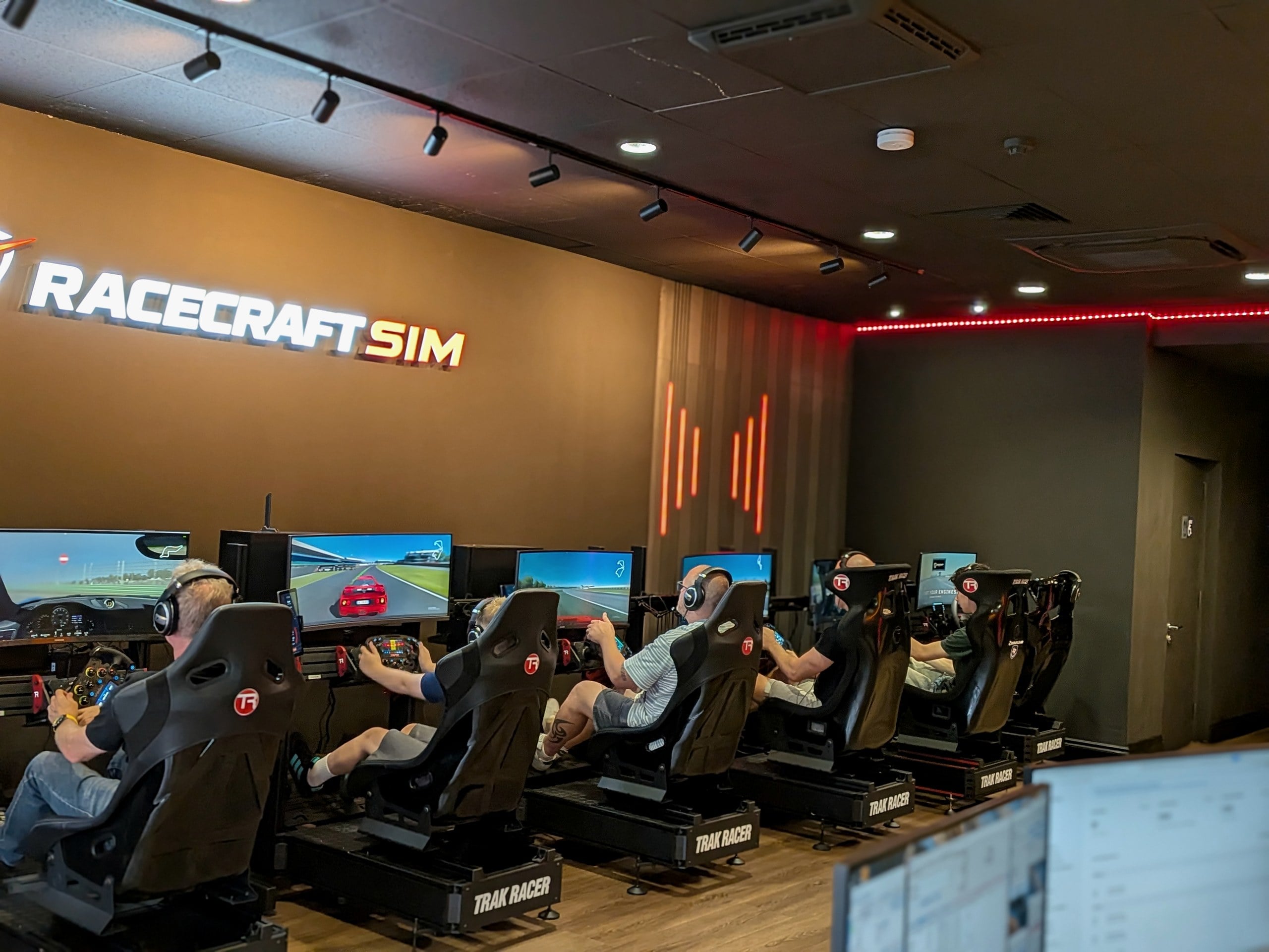 A full grid of drivers racing side by side under the Racecraft Sim logo wall