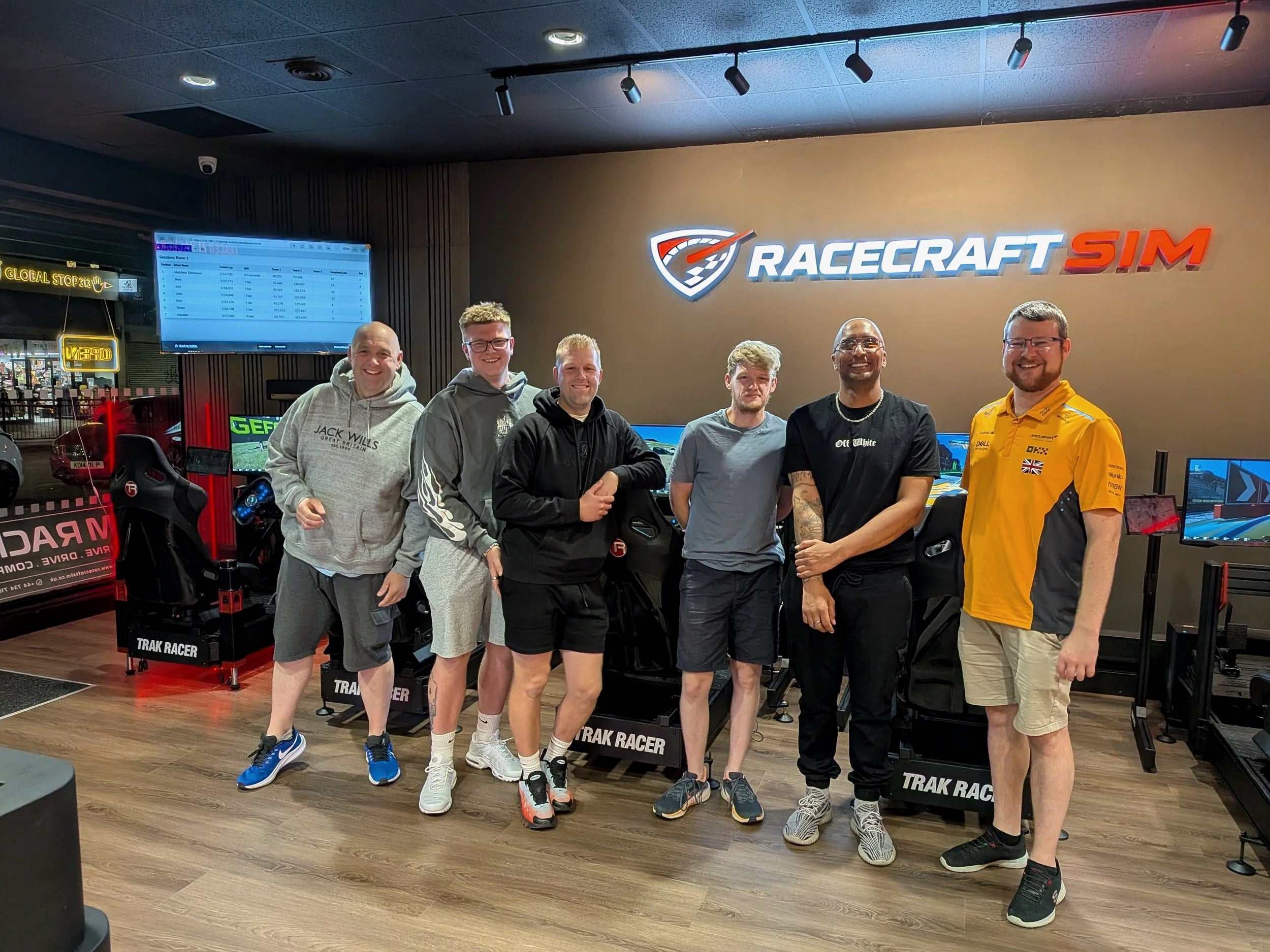 A corporate team posing in front of the Racecraft Sim logo wall